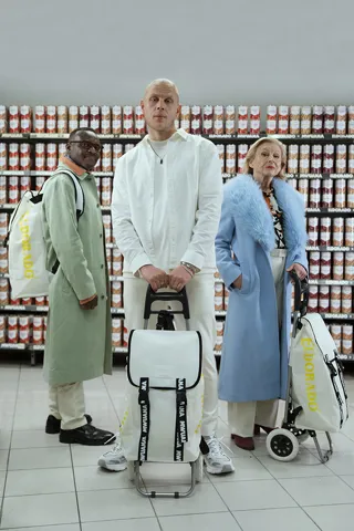 Män och kvinnor med vita dramatenväskor framför hylla med konservburkar